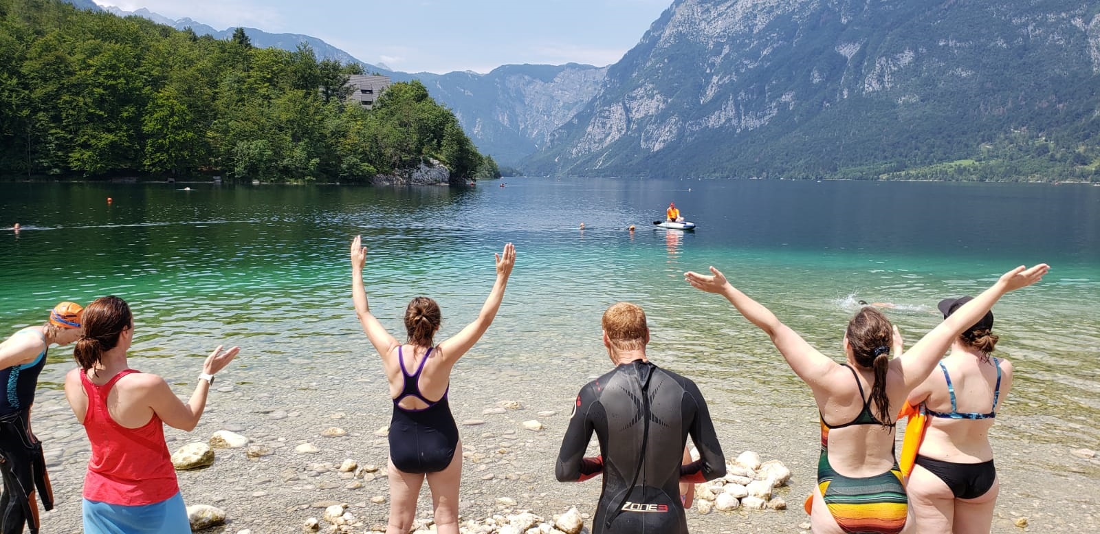 people on the shore of the lake clapping as 2 swimmers (heads) come up to shore with a kayaker by their side.