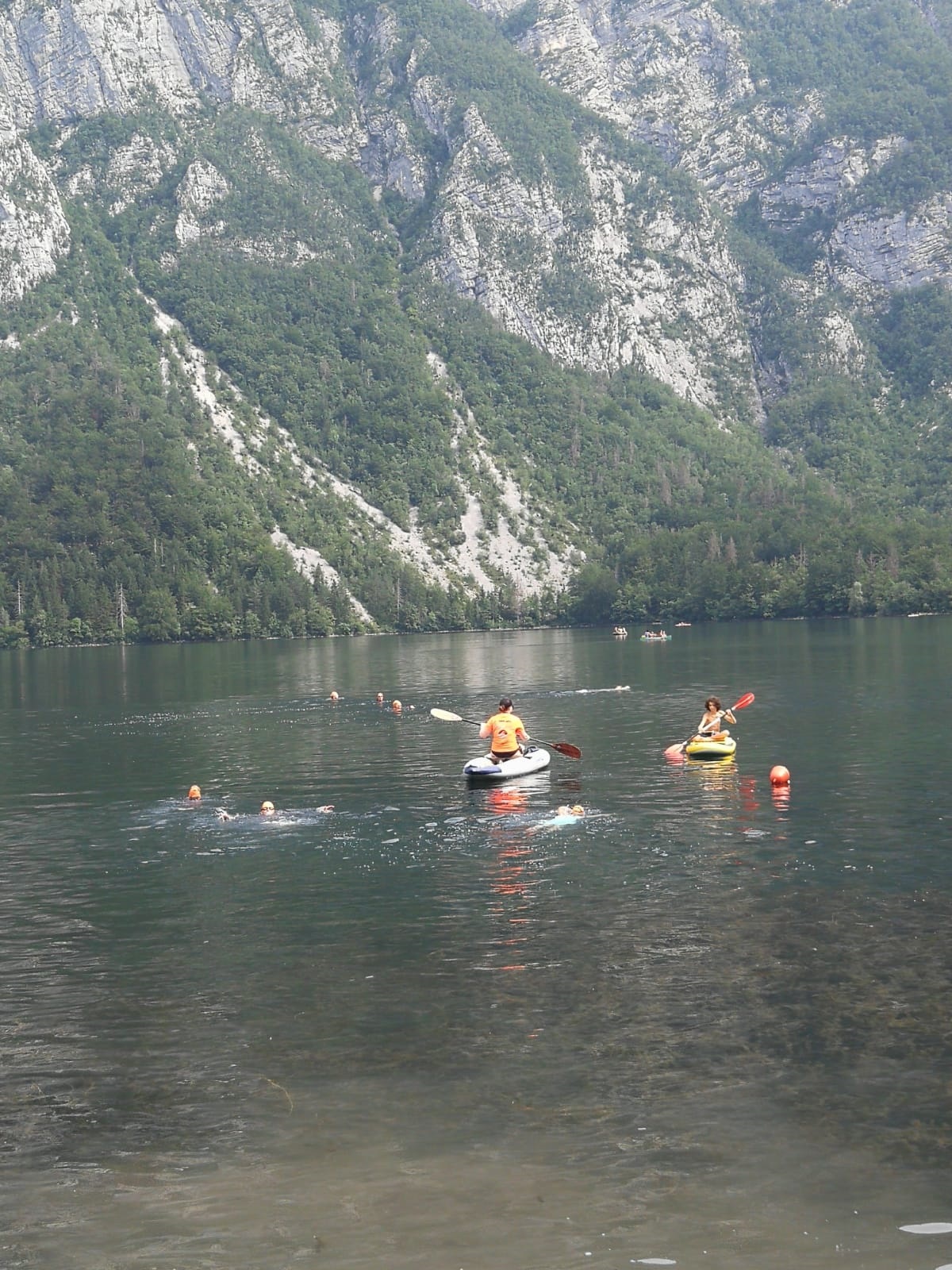 two kayakers with a few swimmers in a lake with a mountain