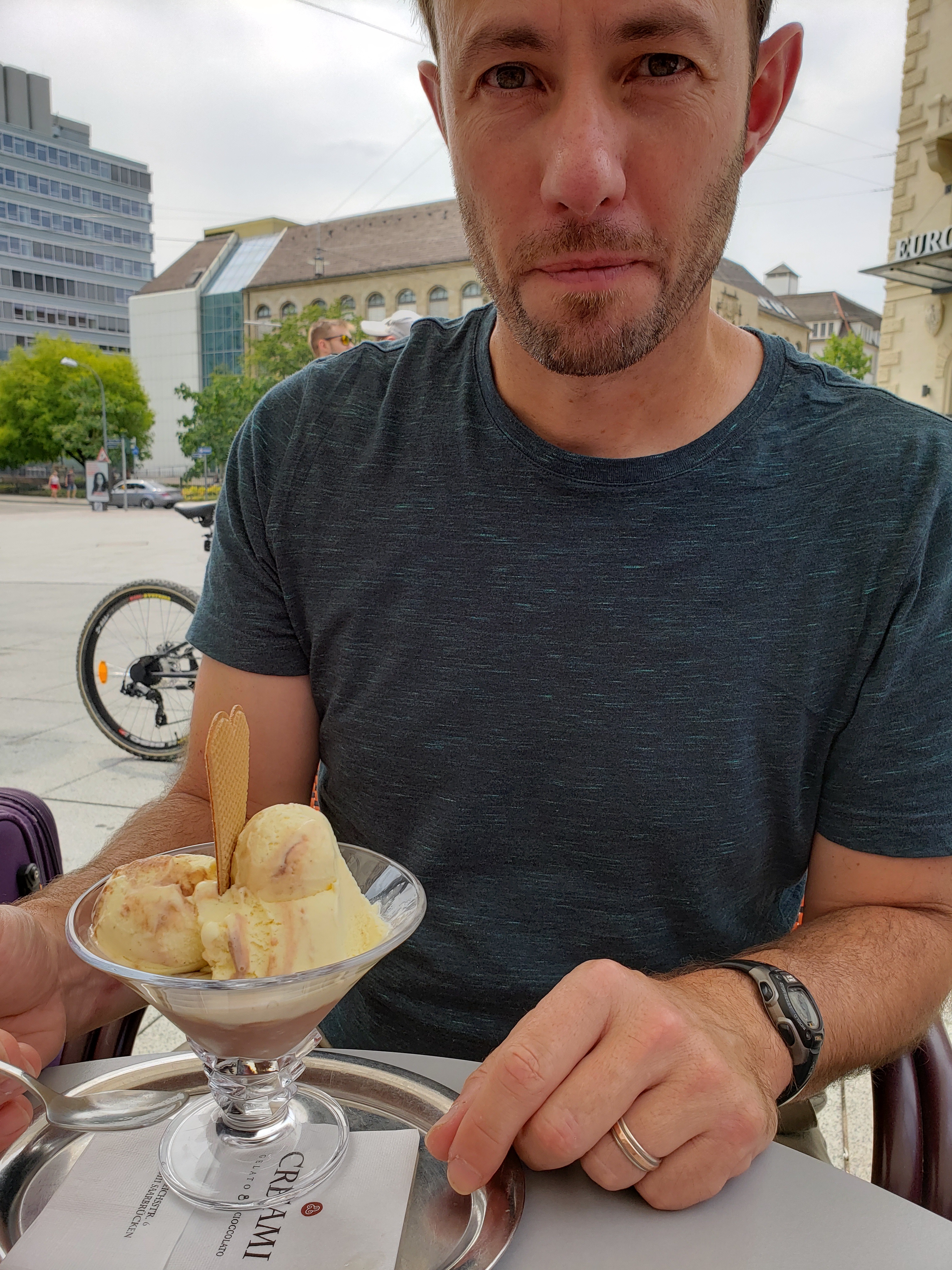 Patrick is wearing a dark green t-shirt seated in front of a martini glass filled with ice cream topped of with a little heart-shaped wafer cookie.