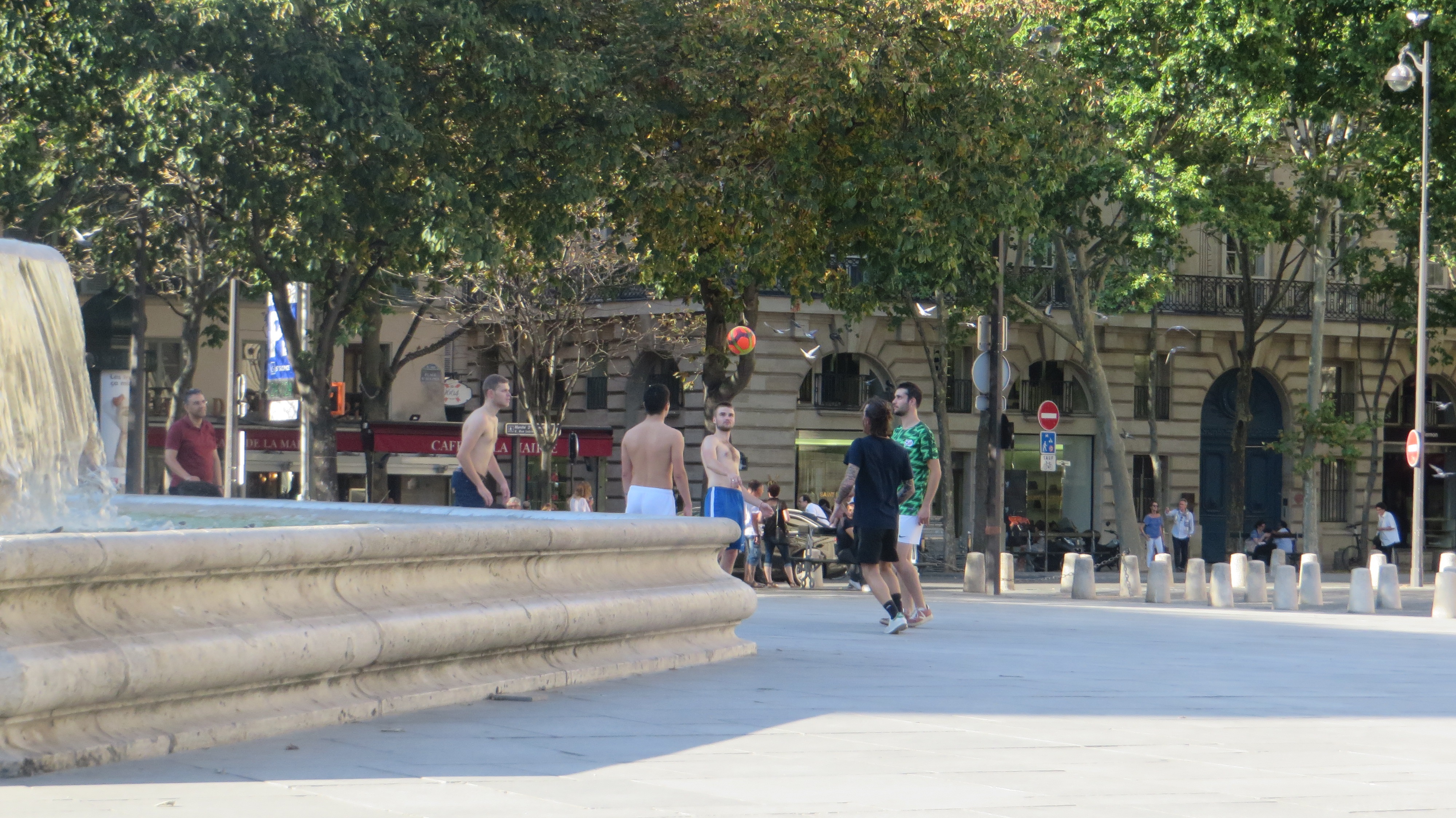 Guys kicking a soccer ball by the fountain.