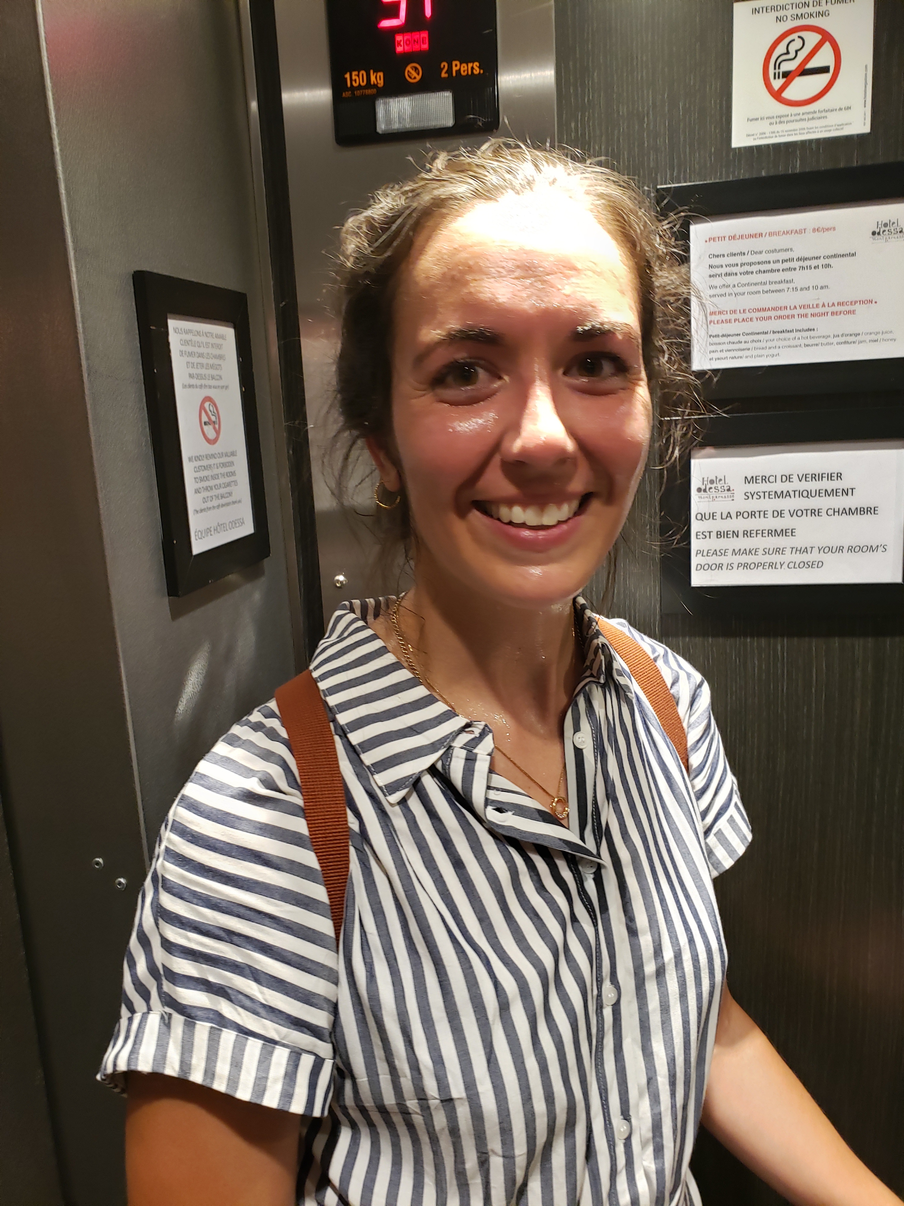 Me in the elevator covered in sweat. Wearing a blue and white striped button down shirt dress and my trusty backpack.