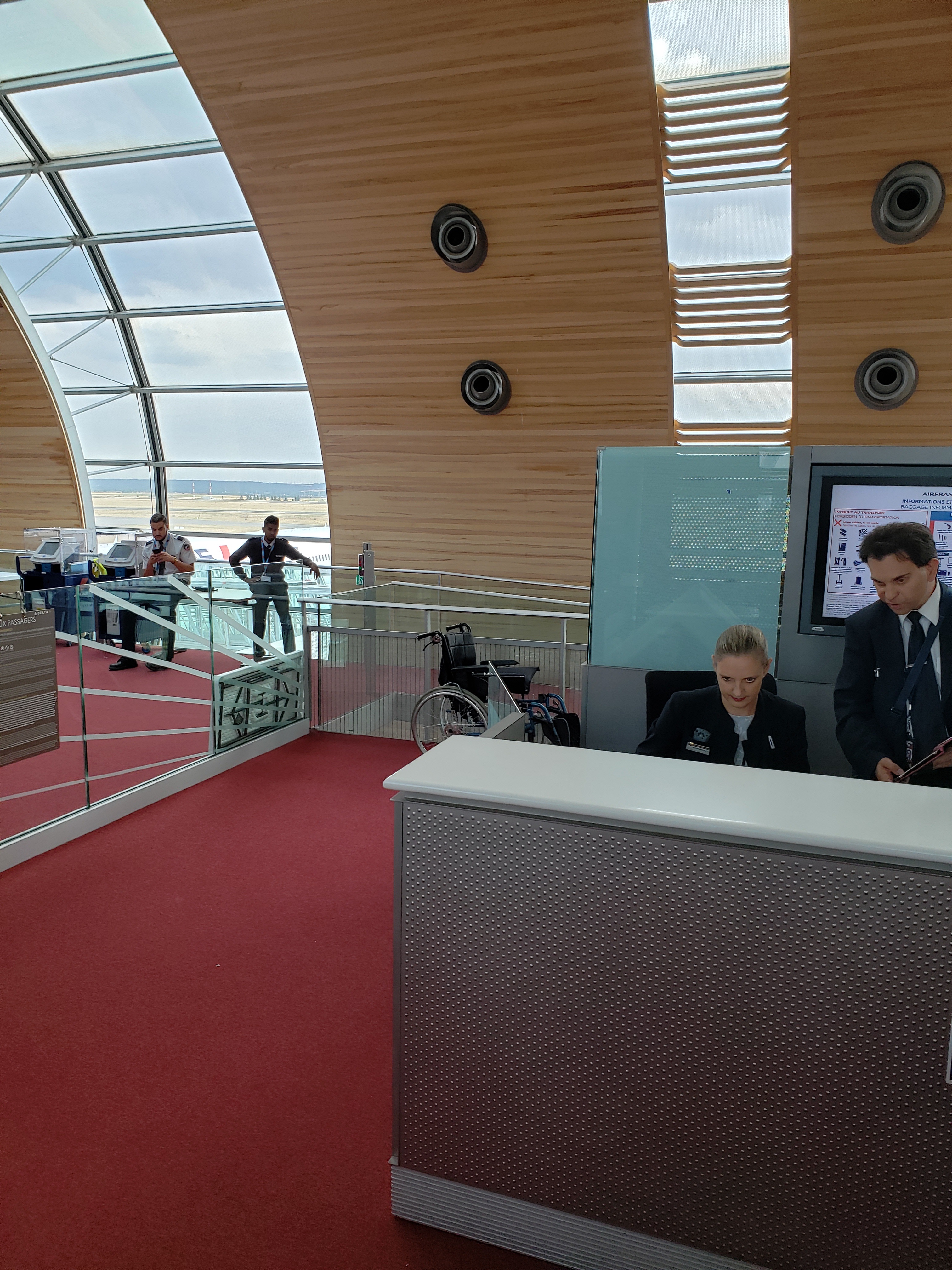 At the airport gate. Two gate agents behind the desk looking at something. Behind them is a wheelchair