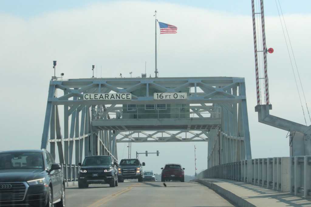 Bridge with cars passing on it and an American flag waving on top.